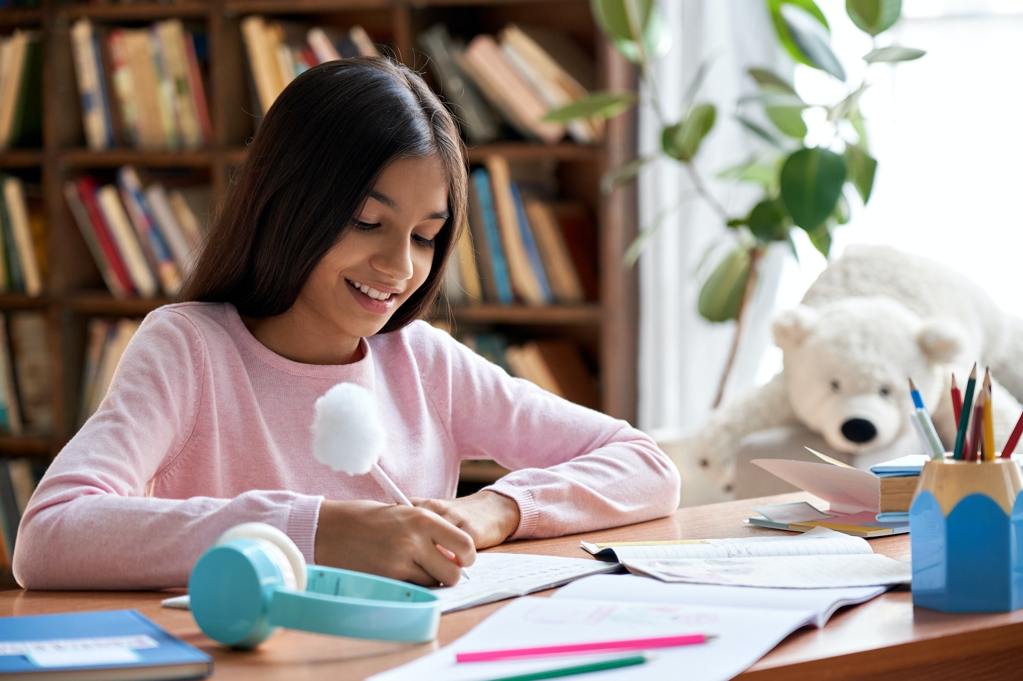 Happy indian latin kid school girl pupil studying at home sitting at desk.