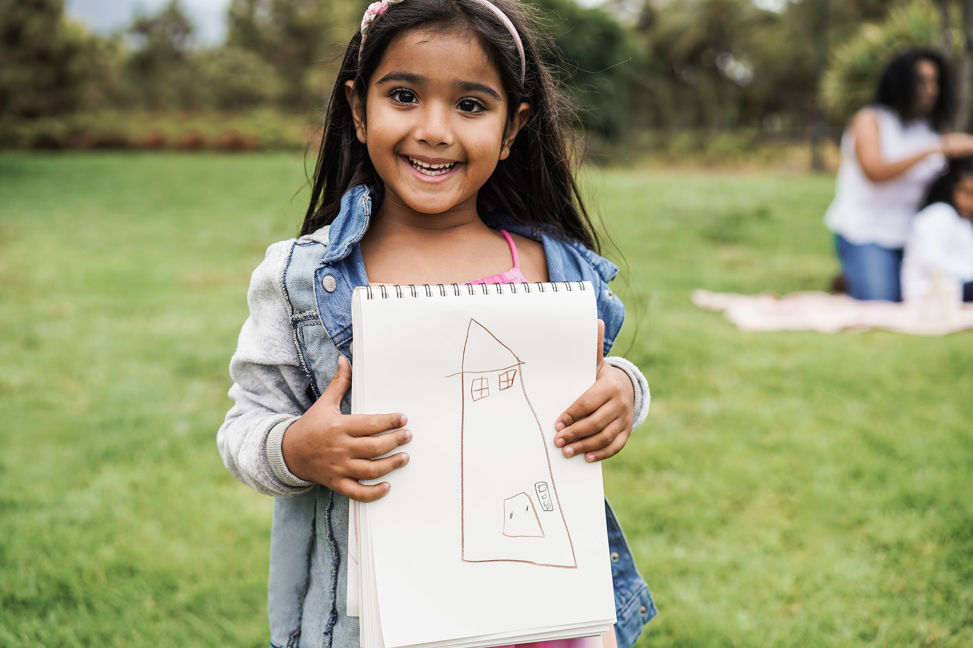 Portrait of indian female kid holding drawing book at city park - Focus on face